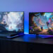 Deux consoles de jeu modernes posées sur un meuble gaming, avec un écran affichant un univers fantastique coloré en 4K et une interface visuelle sobre, dans une ambiance lumineuse bleue et violette.